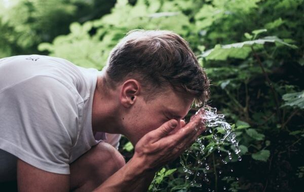 Egy fiú vízzel locsolja le az arcát
