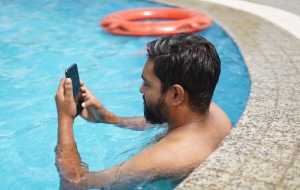 Férfi nyomkodja a telefonját egy medencében